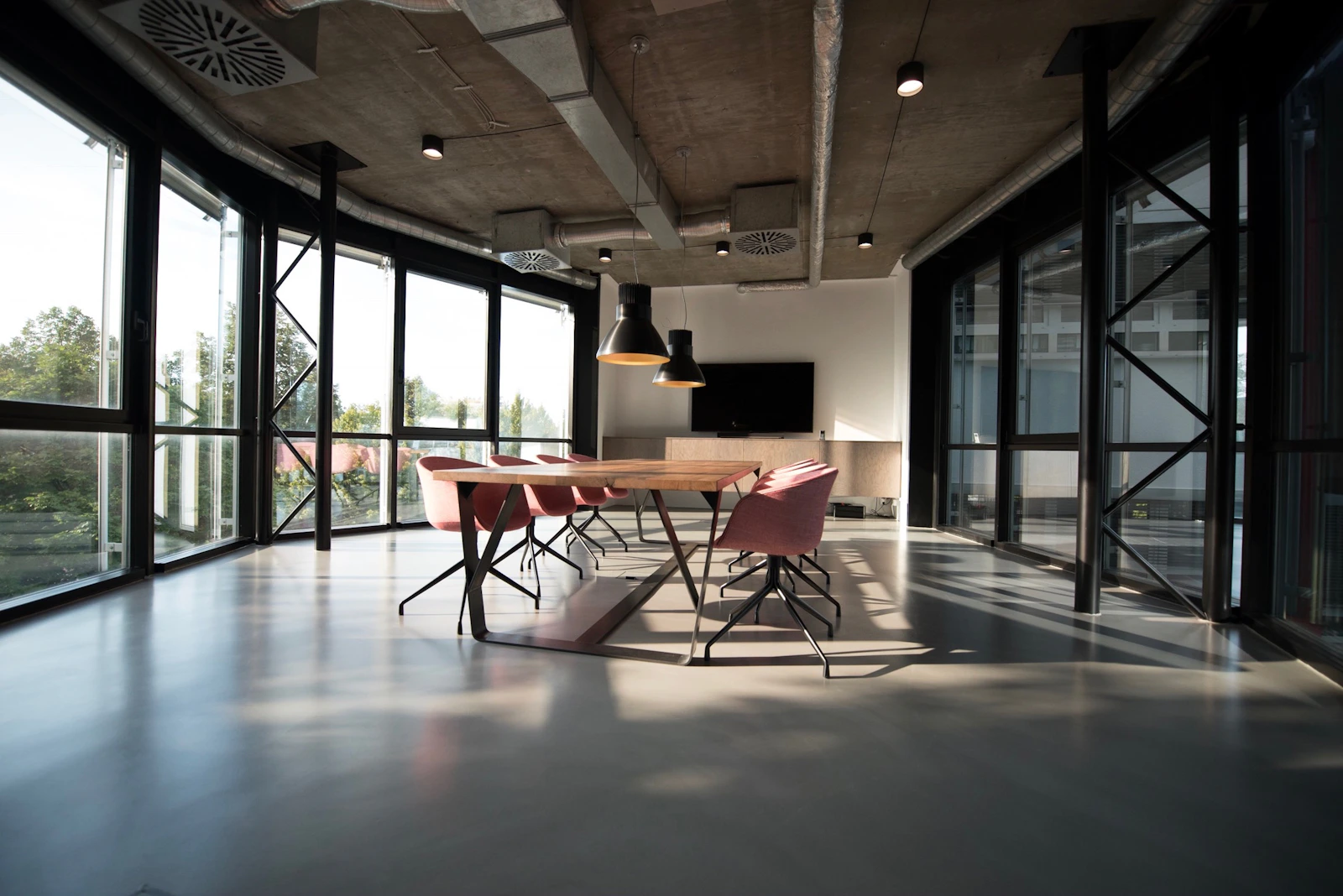 Sala de trabalho do estúdio com mesas longas, cadeiras e bastante luz natural